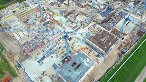 Aerial-Bird-Eye-View-Of-a-Construction-Site-Building-Cranes-Looking-Down-Industrial-Machinery-Area-around-Residential-Urban-Apartments