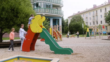 Little-girl-with-down-syndrome-playing-with-other-kids-in-the-park-on-a-windy-day.-They-are-getting-on-slide