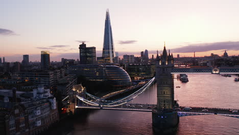 Ascending-evening-footage-of-Tower-Bridge-over-River-Thames.-modern-building-of-city-hall-and-Shard-skyscraper-on-bank.-Water-surface-reflecting-pink-twilight-sky.-London,-UK