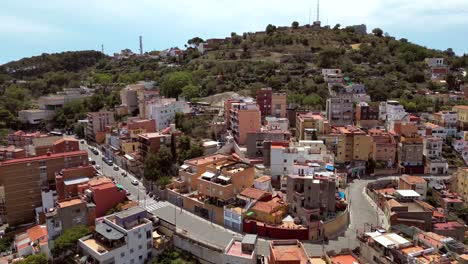 Eine-Filmische-Zeitlupen-Drohnenaufnahme-Der-Stadt-Barcelona-Mit-Hohen-Und-Niedrigen-Gebäuden-Und-Telekommunikationstürmen-In-Der-Ferne