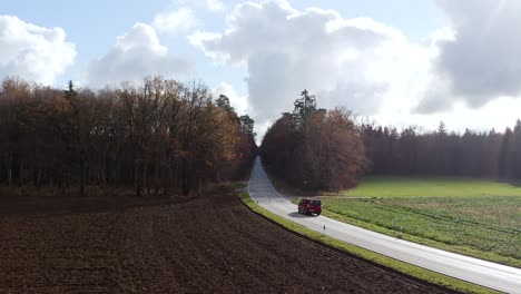 Driving-car-through-a-curve-leading-into-a-autumn-colored-forest-from-lower-aerial-position