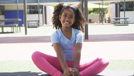 Una-Chica-Birracial-Con-Pelo-Rizado-Se-Sienta-Sonriendo-En-Un-Patio-De-Escuela