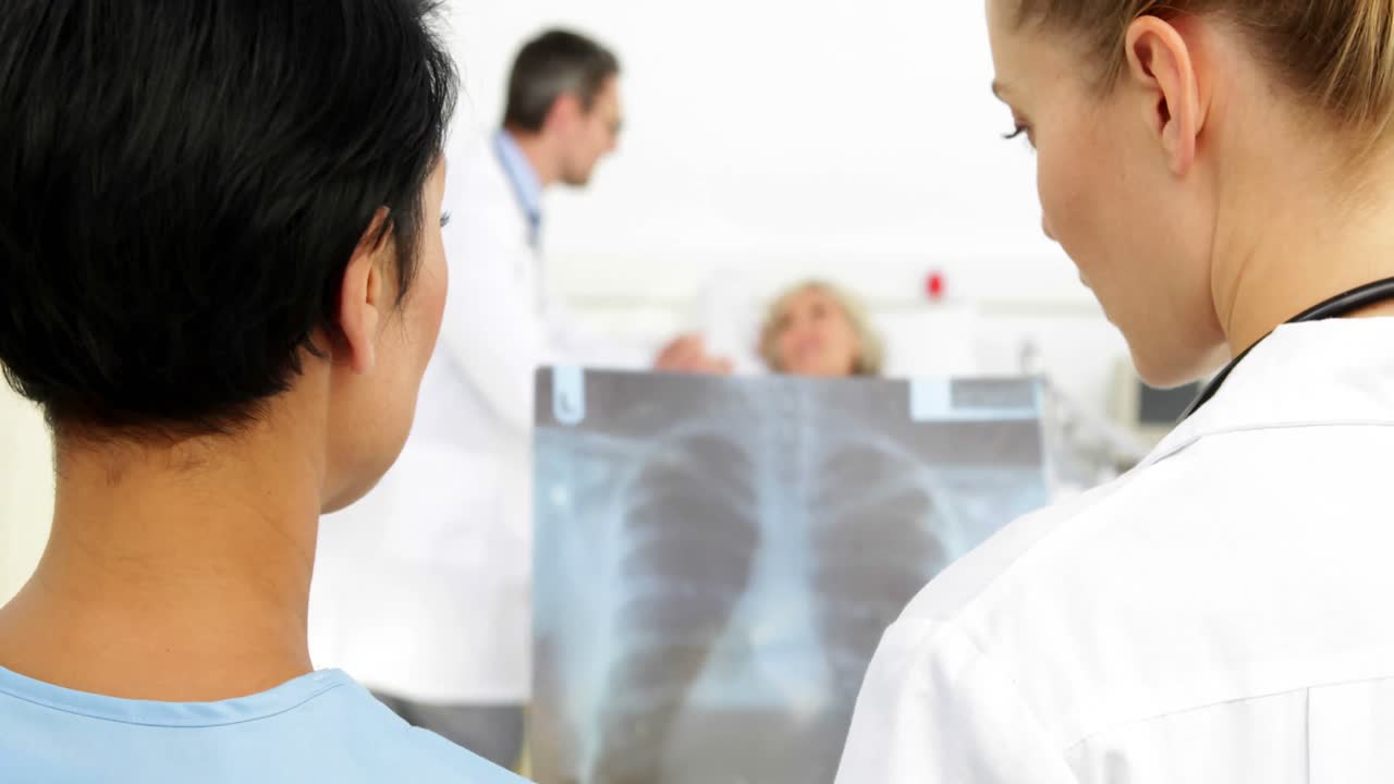 médicos discutiendo rayos x frente a un paciente enfermo en la cama