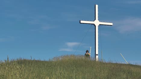 a woman walks toward a large white cross on top of a hill