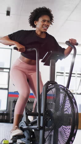 vertical video of determined african american woman working out at a gym on exercise bike