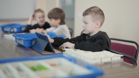 children intently focused on assembling parts from a robotics kit, with a tablet displaying instructions, promoting stem learning and creativity