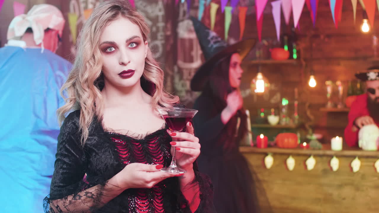 Halloween party with a woman in vampire costume drinking a cocktail