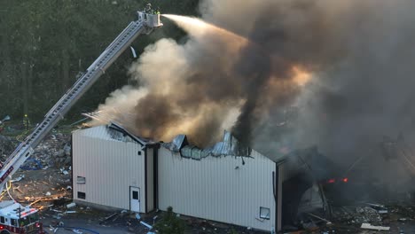 Firefighter-on-ladder-extinguish-fire-after-gas-explosion-during-daytime-in-American-city---dark-toxic-fumes-rising-up-in-nature---aerial-zoom-wide-shot