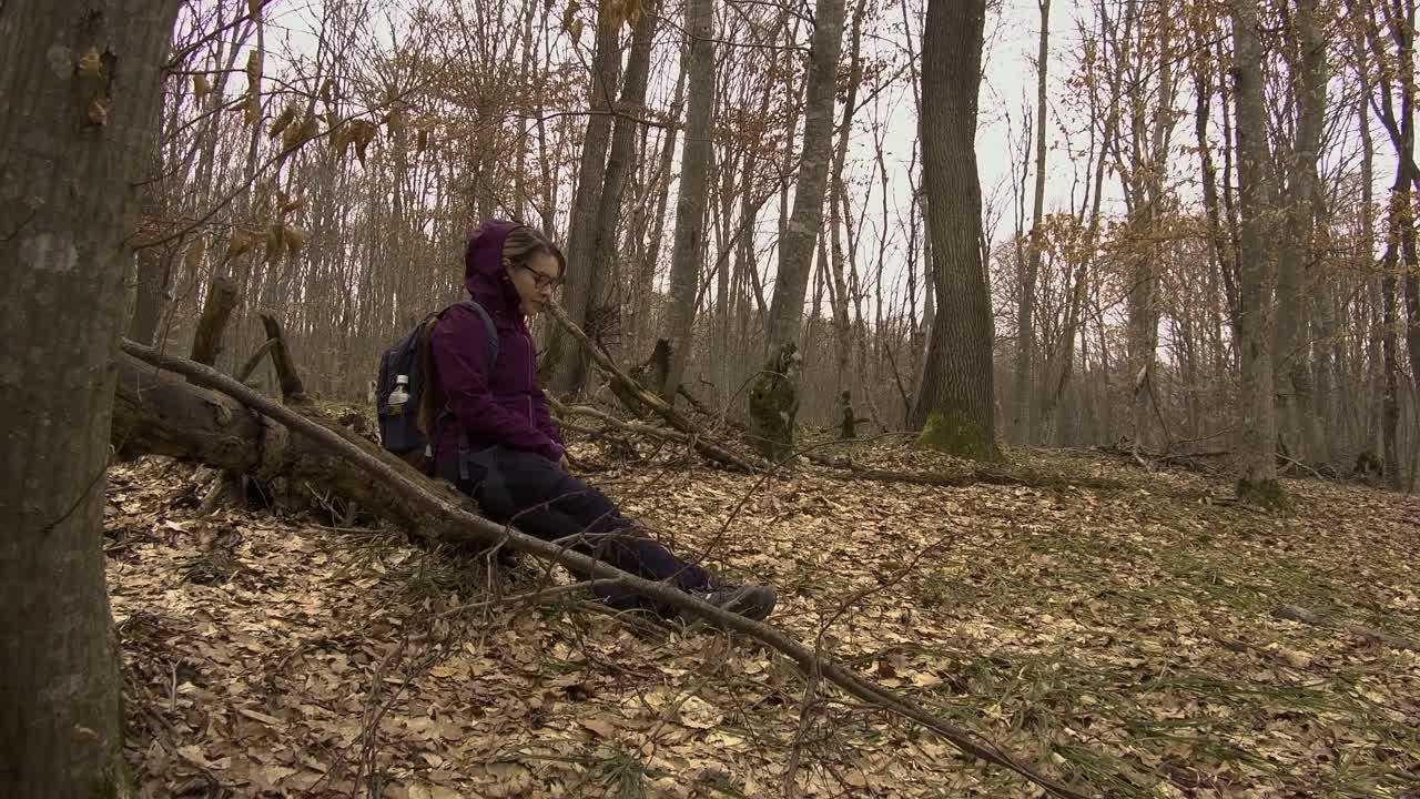 Low angle side view of woman in forest sitting on a fallen tree to rest
