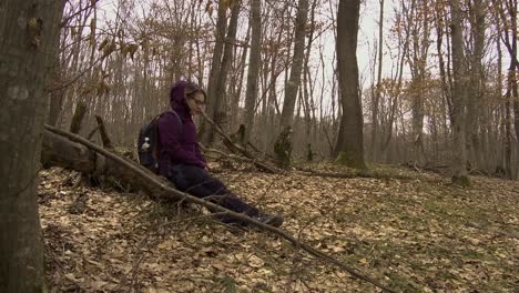 low angle side view of woman in forest sitting on a fallen tree to rest