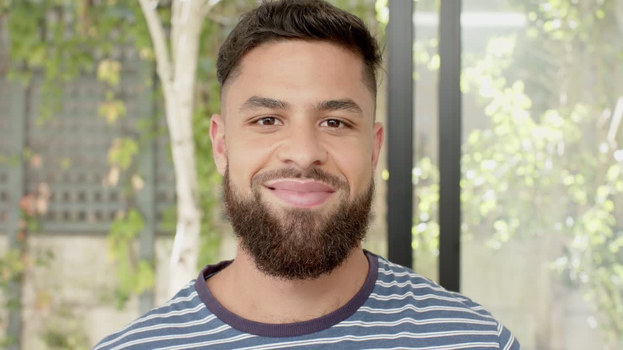 Smiling young man with beard wearing striped shirt, standing outdoors
