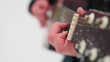 close-up of hand playing guitar strings in winter setting, highlighting frosted details on strings and fingerboard, vibrant contrast between hand's warmth and cold snowy background