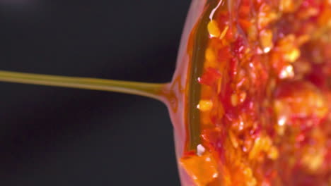 Antigravity-horizontal-perspective-of-isolated-colorful-traditional-authentic-sambal,-oily-chili-paste,-dripping,-pouring-down-from-clear-glass-bowl,-black-background,-extreme-close-up-static