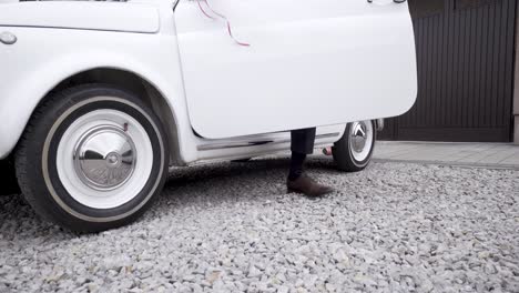 well dressed man in suit getting out of white classic car