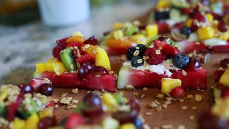 panning shot over slices of watermelon with a yogurt cream on top along with granola and a variety of fruits including blueberries, pineapple, strawberries, and raspberries