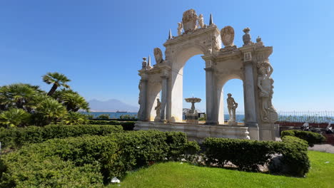 elegant arch del sebeto and statues in a sunlit garden with a stunning view of the sea and mount vesuvius in the distance