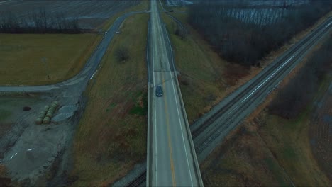 a car travels on an overpass over railroad tracks near a lake in rural southern illinois with some light snow on the ground