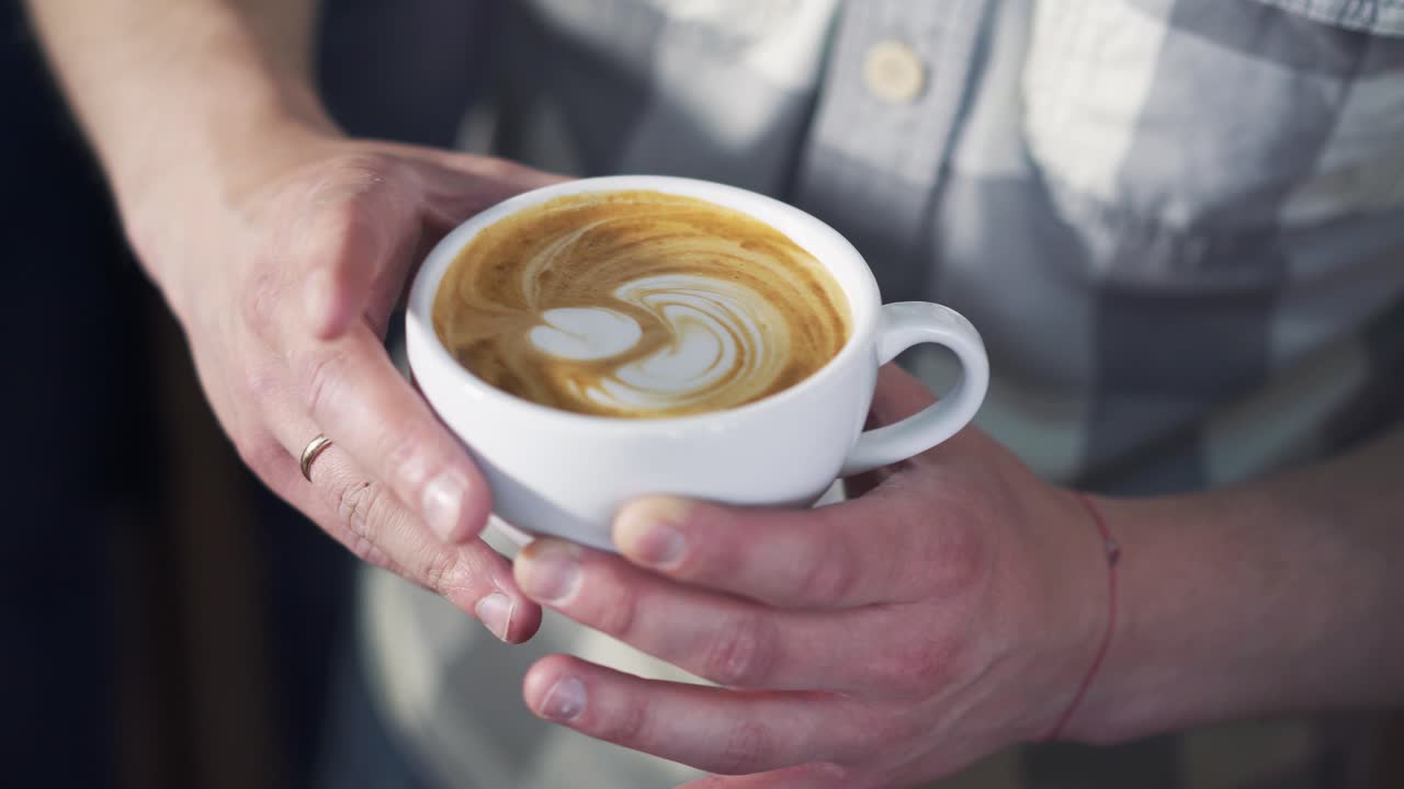 Professional barista pouring milk foam over coffee into white cup creating perfect cappuccino and making a nice pattern