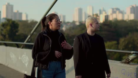 two friends walking and talking on a city bridge during the day