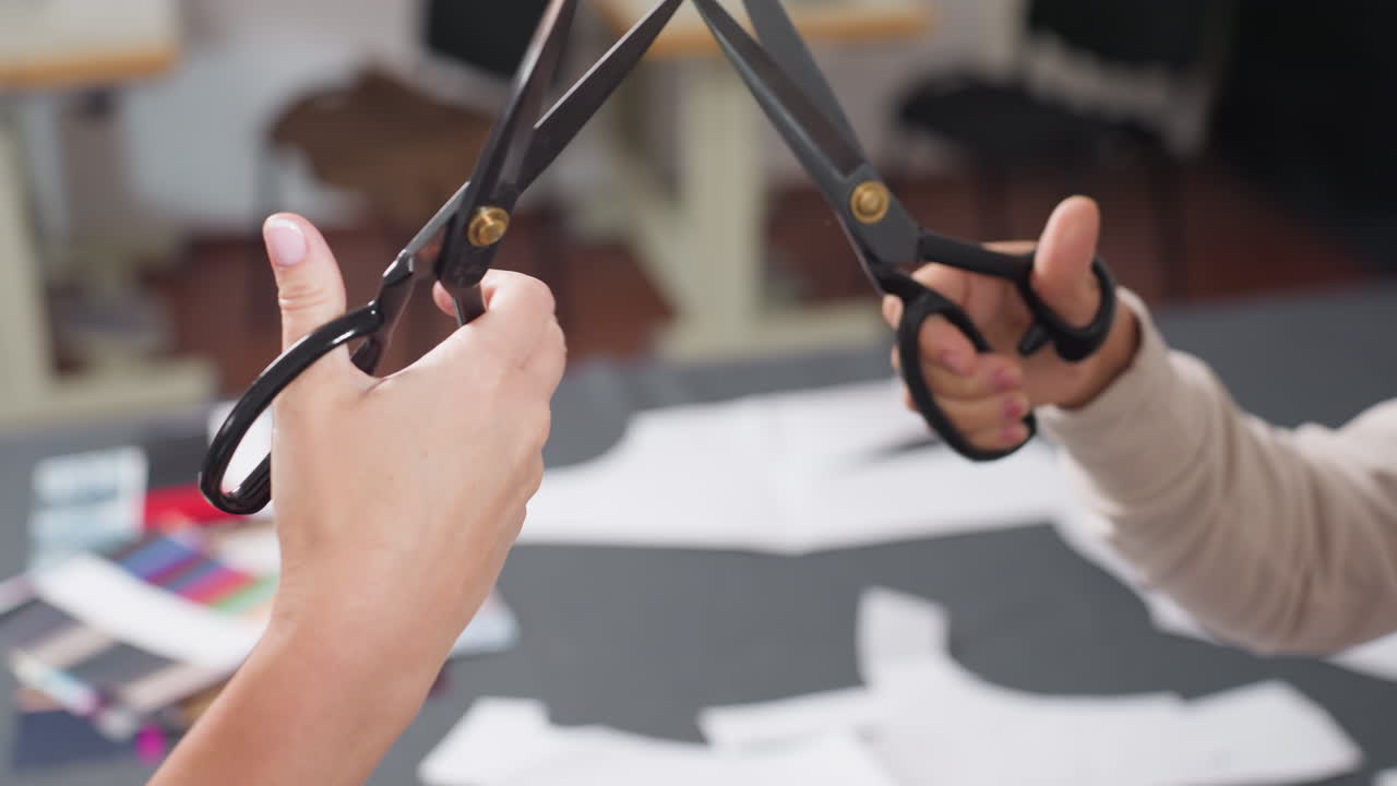 Creative hands holding scissors engaging in playful cutting fight above work table scattered with colorful fabric samples and sewing patterns, dynamic workspace, expressing energy and collaboration