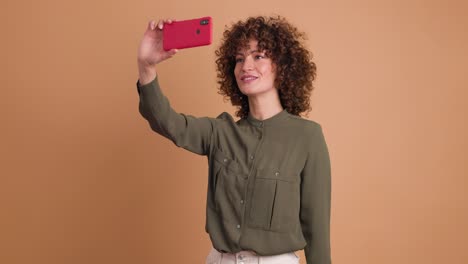 cheerful woman taking self pictures with mobile phone on beige background