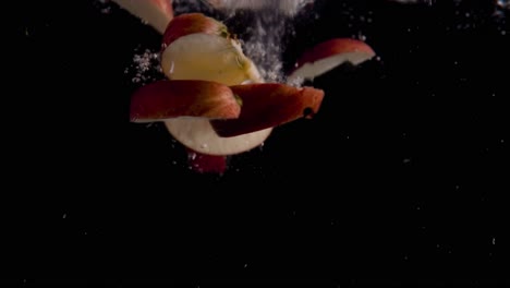 rebanadas de manzana cayendo en cámara superlenta de agua, fondo negro, muchas burbujas de aire, 4k240fps