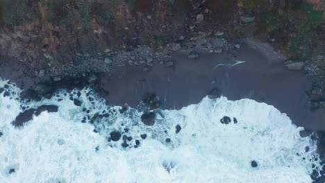 top-down aerial of white ocean waves breaking on rocky shore, california