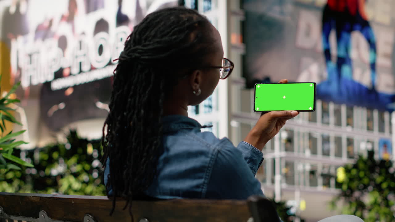 Sort pige slapper af på parkbænk med chroma key telefon