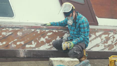 un hombre lijando las tablas de caoba de un casco de barco de madera