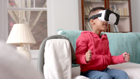 niño afroamericano usando auriculares vr y tocando pantalla virtual en la sala de estar, cámara lenta