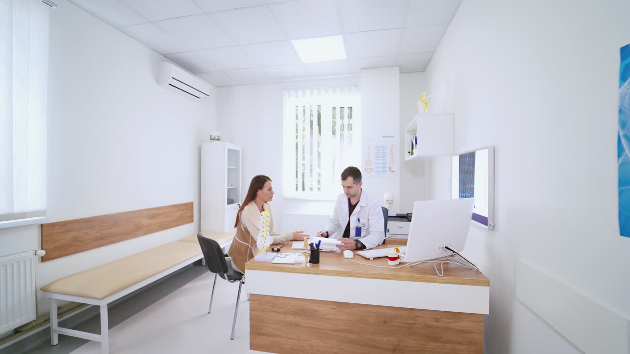Young doctor talking with a patient. Contemporary consulting room in clinic. Attractive female visits medical specialist and talking about her health problems.