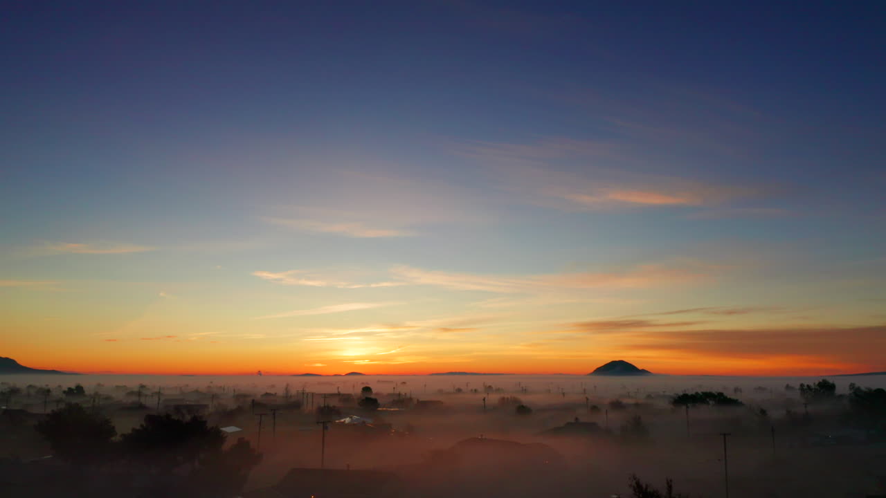 주황색 일출의 전화선과 안개가 자욱한 동네 위로 공중으로 떠오르는 총격