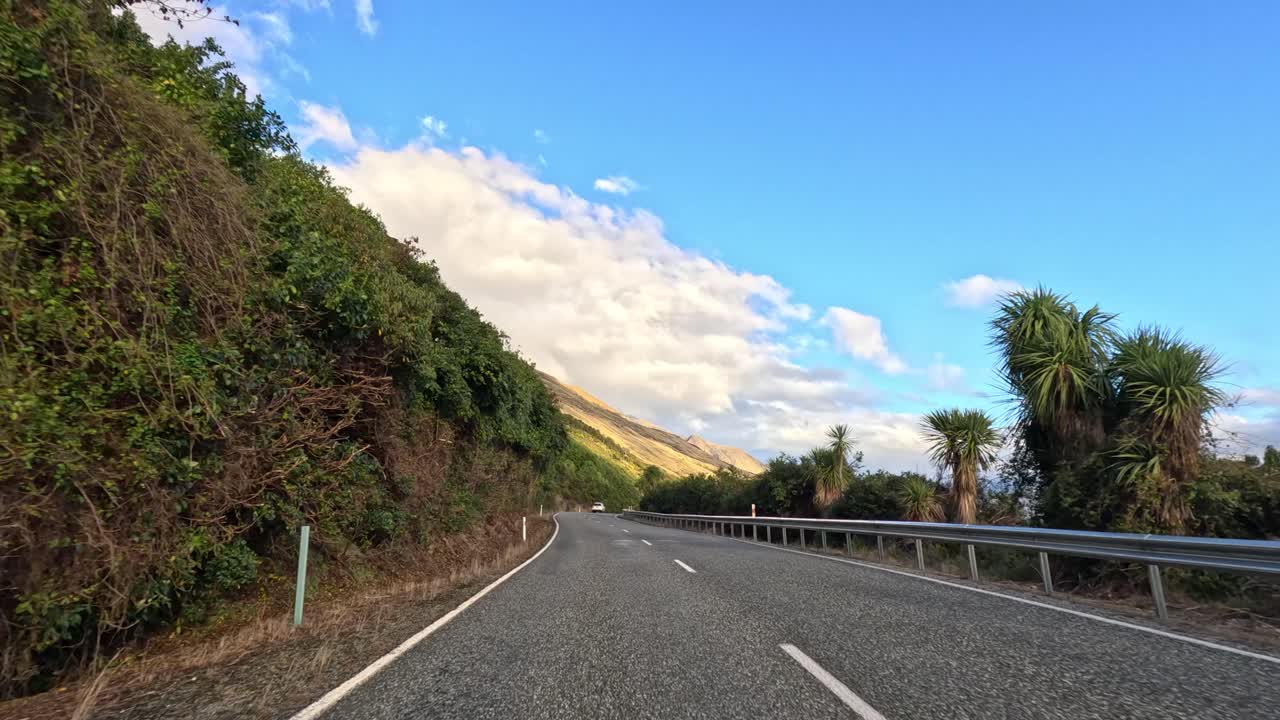 Forward-facing car view on winding rural road, lush greenery, clear sky, natural daylight, smooth motion