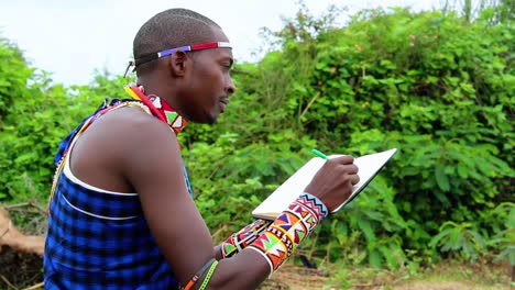 hombre masai escribiendo notas en un libro, sentado al aire libre, en kenia, áfrica