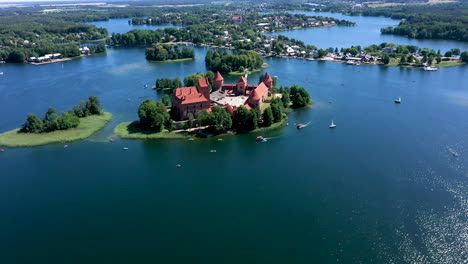 aéreo: toma giratoria a gran altura del castillo de trakai con barcos y yates dando vueltas en el lago alrededor de la isla del castillo de trakai con el sol proyectando reflejos de luz en la superficie del lago