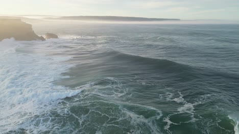 aerial shot over the ocean near the cliffs of nazaré, portugal with soft sunlight.