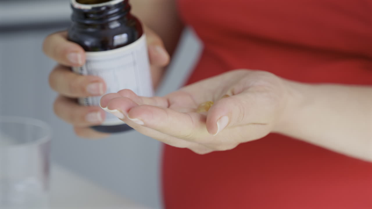 Primo piano di una donna incinta che versa integratori di olio di pesce sul palmo della mano