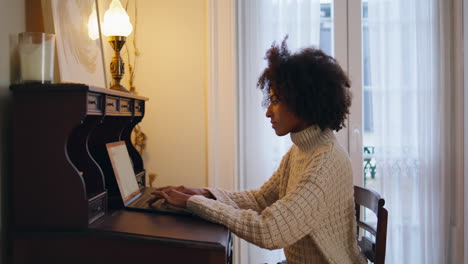 modelo enfocado escribiendo teclado de portátil en casa. mujer africana trabajando en la computadora