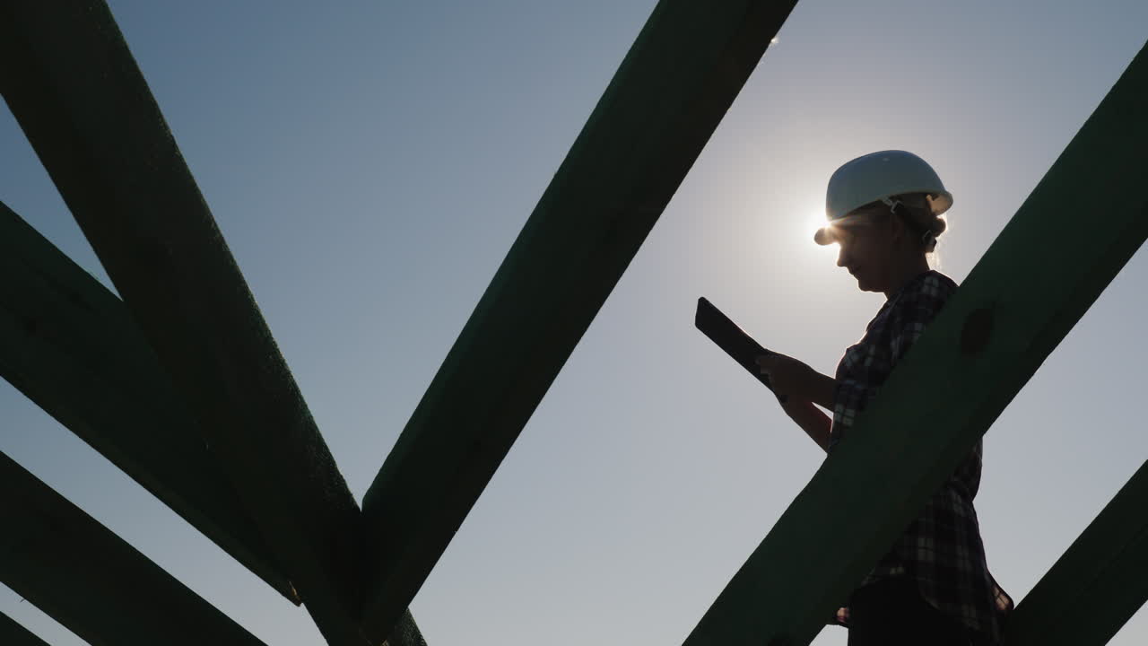una joven ingeniera trabaja con una tableta en el techo inacabado de una cabaña