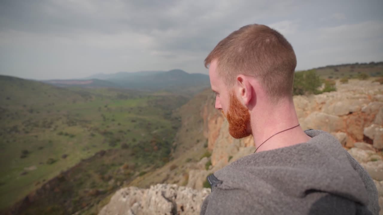 hombre blanco con barba parado en un acantilado en israel mirando hacia el valle, vista de cerca