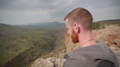 White-male-with-beard-standing-on-cliff-in-Israel-looking-into-valley,-close-up-view