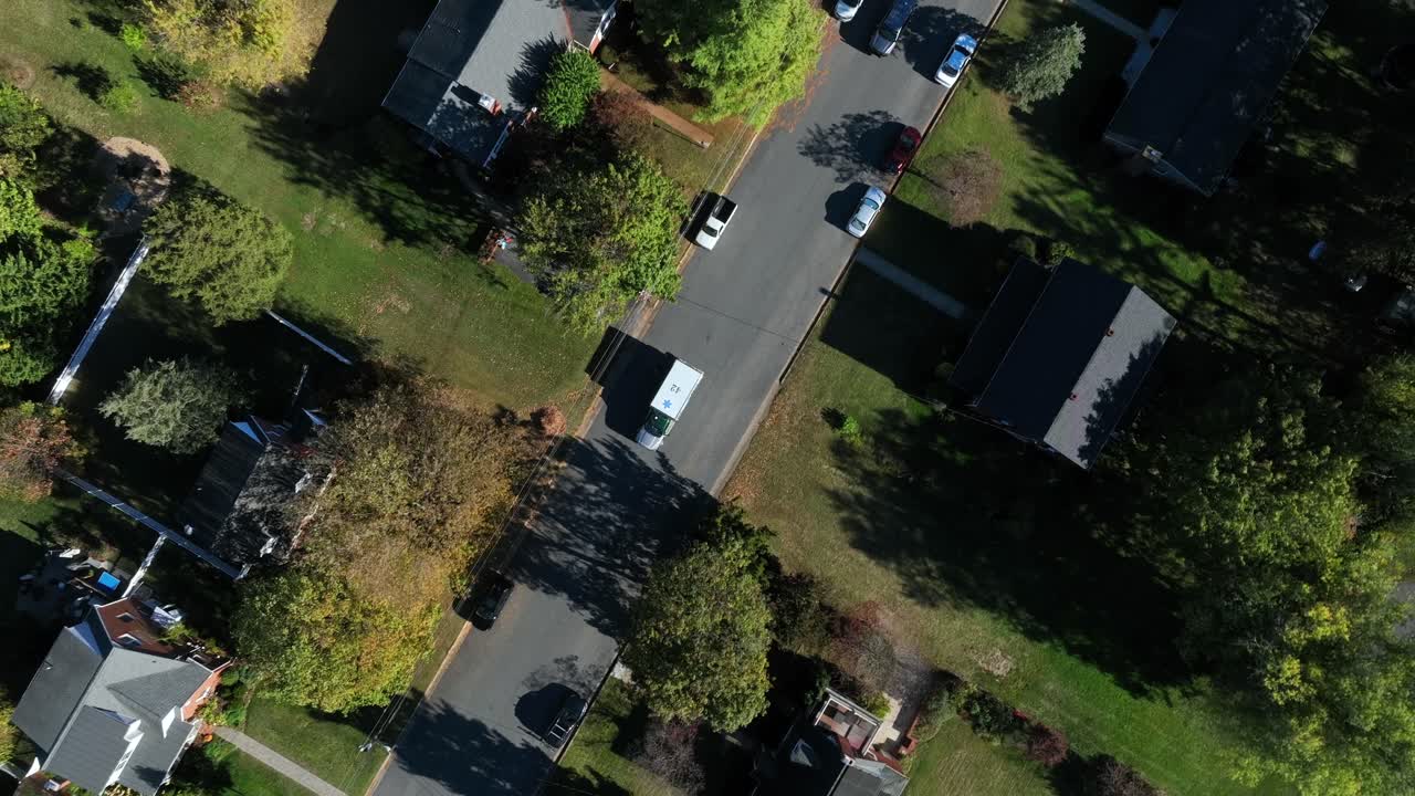 Suburb neighborhood with ambulance vehicle and cars on street between houses and homes. Sunny fall day in USA. Aerial top down circling shot. Housing area with roofs and garden