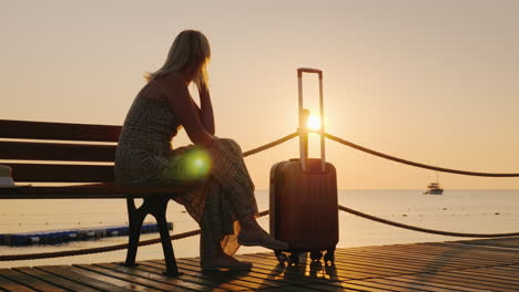 A-Woman-With-A-Travel-Bag-Sits-On-A-Wooden-Pier-Looking-Forward-To-The-Dawn-Over-The-Sea-And-A-Ship-