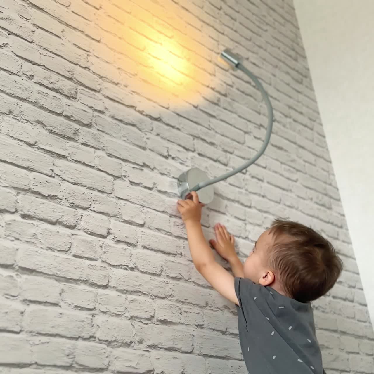 Happy toddler switching on the light on the wall. Adorable kid is smiling playing with the lamp. Low angle view