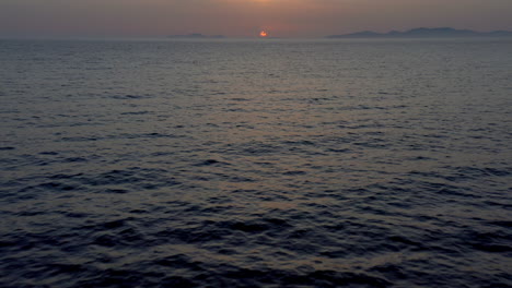 aerial: backwards tilt reveal drone shot that flies low over the sea during sunset