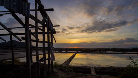 Reflejo-De-Espejo-Al-Atardecer-En-Los-Campos-De-Sal-Con-Cobertizo-En-Ruinas-En-Primer-Plano