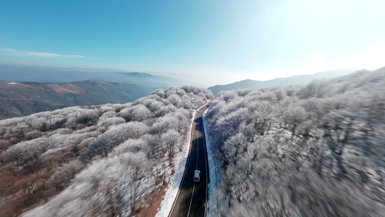 Snow-covered trees and a winding road seen from a drone flying above the mountains
