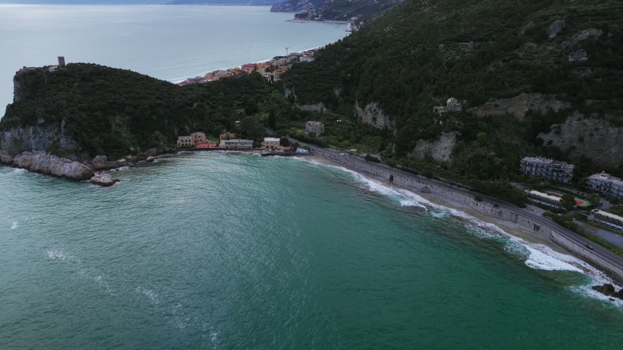 Picturesque Noli village, beach, bay, green hills on Ligurian coast, Italy. Aerial forward tilt-up reveal, copy space