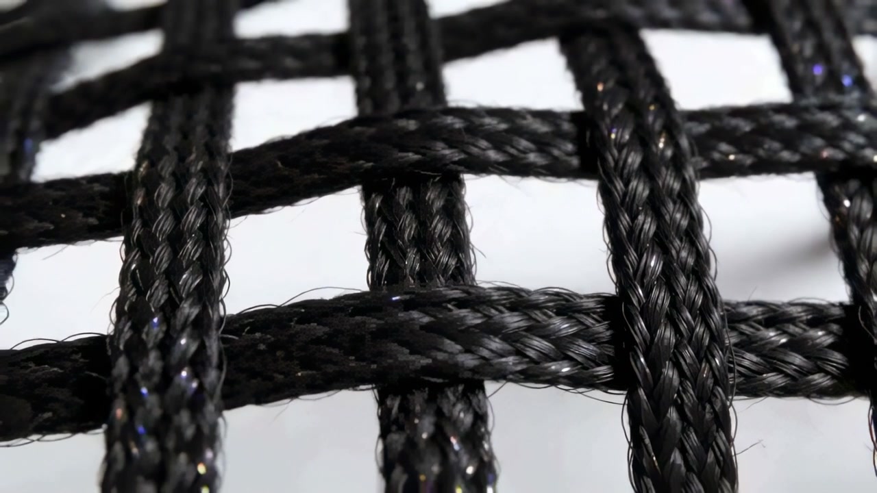 Moving camera revealing black braided cord grid on white sheet, highlighting iridescent strands