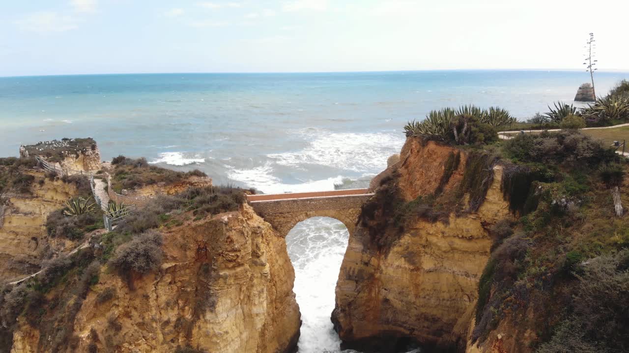 Stone Bridge connecting eroded cliffs in Student Beach In Lagos, Algarve, Portugal - Aerial dronie ascending wide view shot
